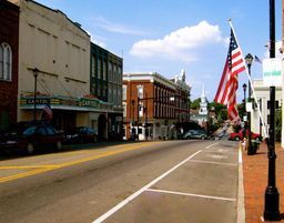 Street scene in a small town, with buildings, a movie theater, US flag, and parked cars under a blue sky