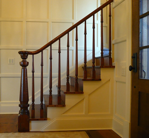 Wooden staircase with dark brown banister and steps, white wall paneling