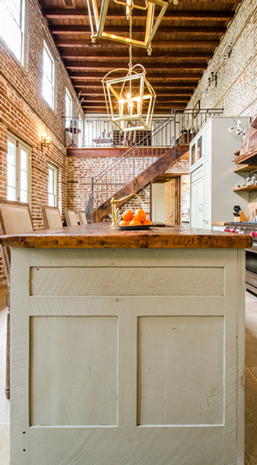 Loft interior with exposed brick walls, wooden floors, and a kitchen island, bathed in sunlight
