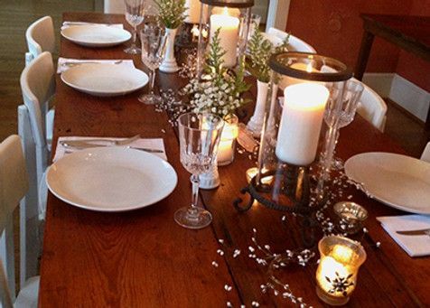 A long, wooden dining table set for a formal dinner, candles and flowers in the center