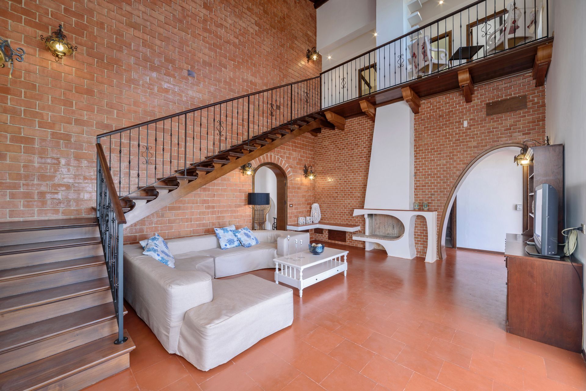 Living room with brick walls, staircase, sofa, fireplace, and mezzanine