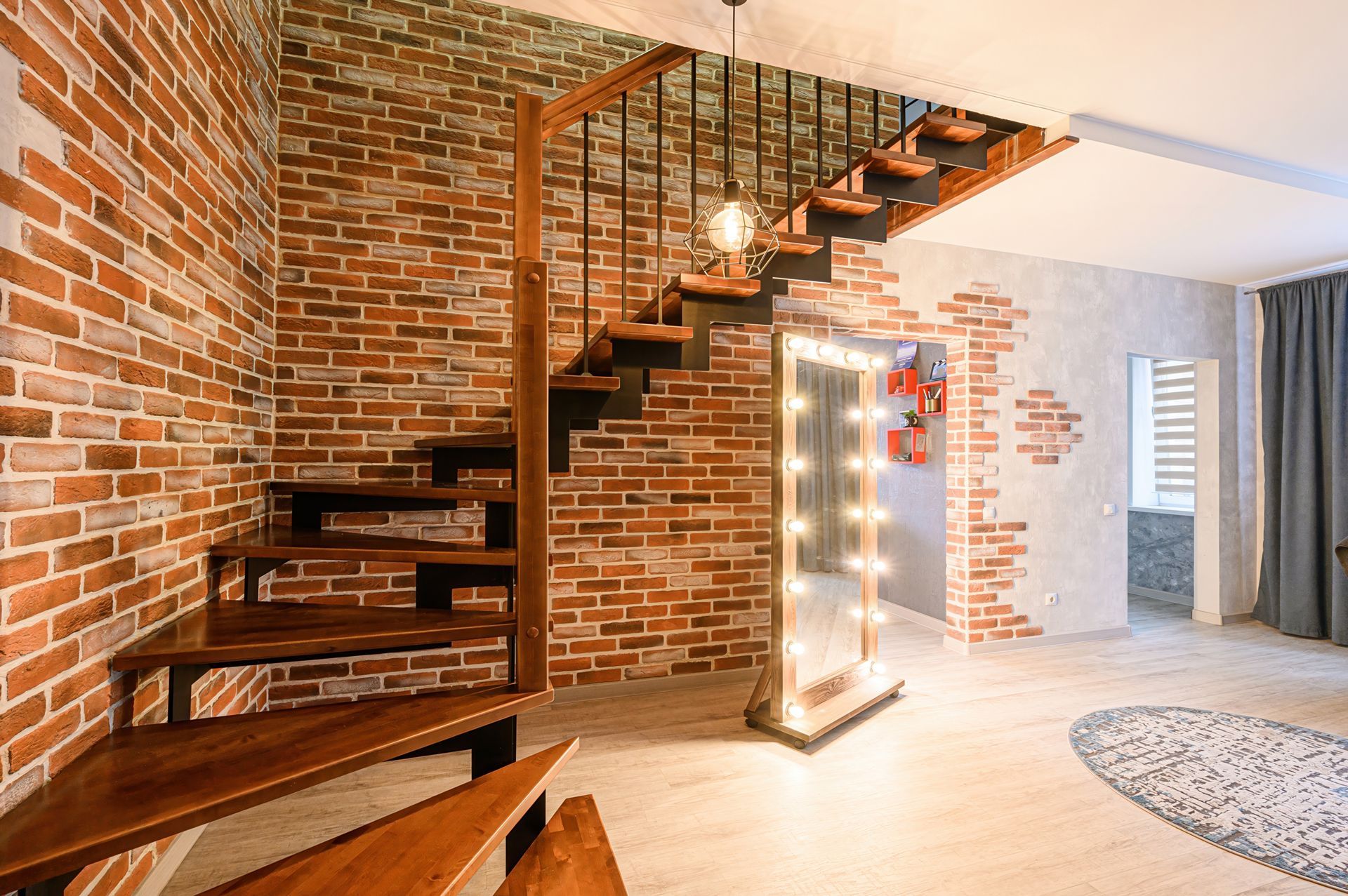 Brick-walled interior with wooden staircase, large mirror, and round rug