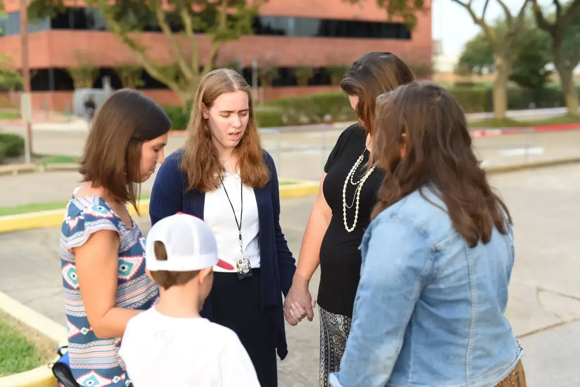 People holding hands in a circle, praying outside a building.