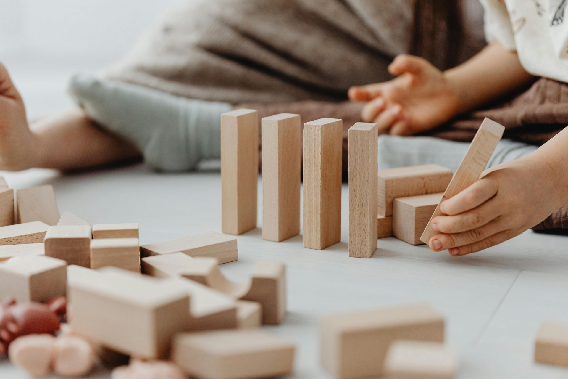 Child playing with wooden blocks on a white floor.