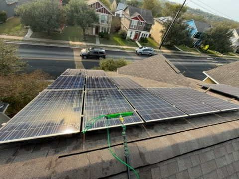 Solar panels on a roof, with a cleaning tool.  Street and houses in the background.