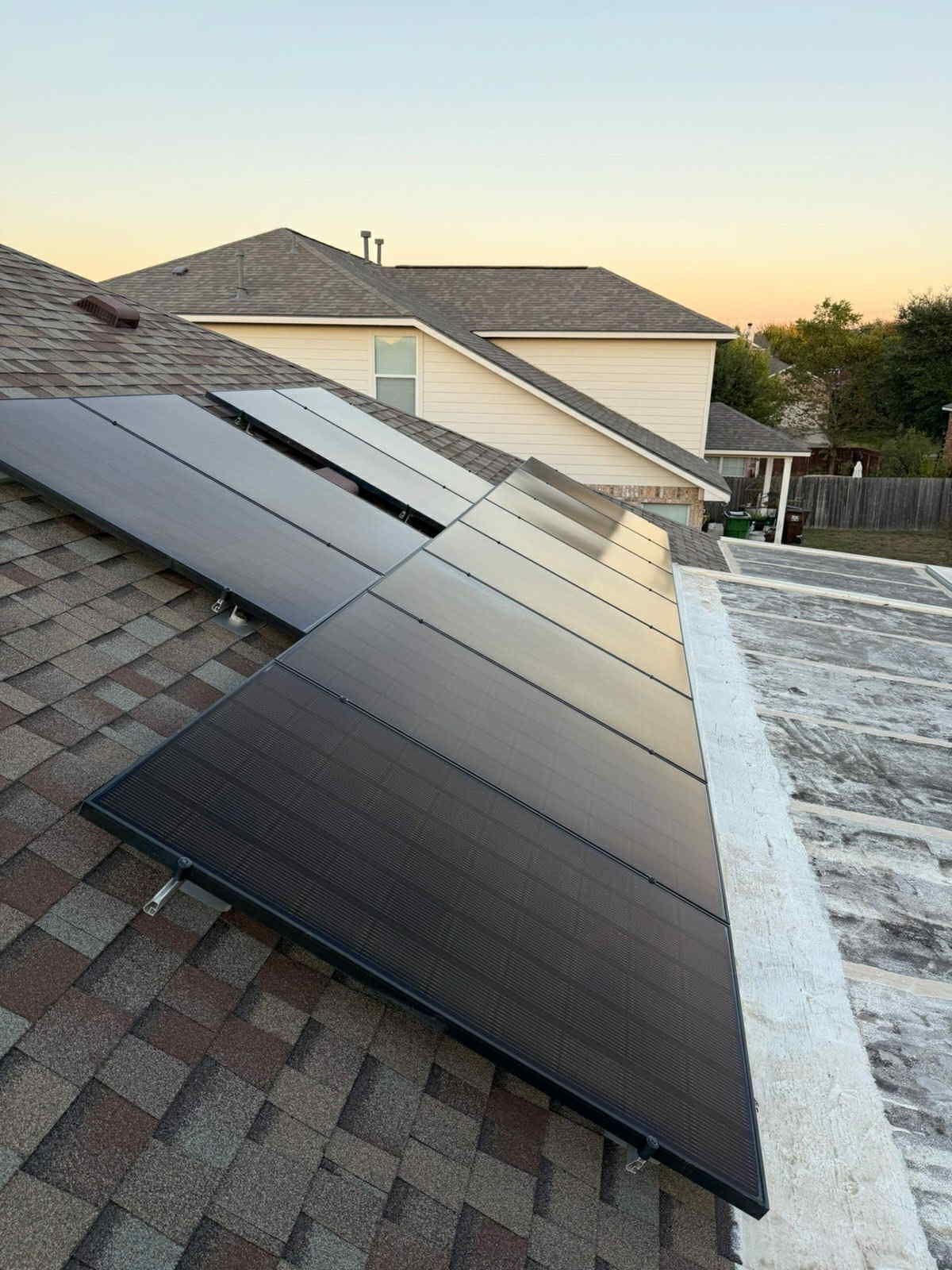Solar panels installed on a residential rooftop. Brown shingles, white trim, and a clear sky in the background.