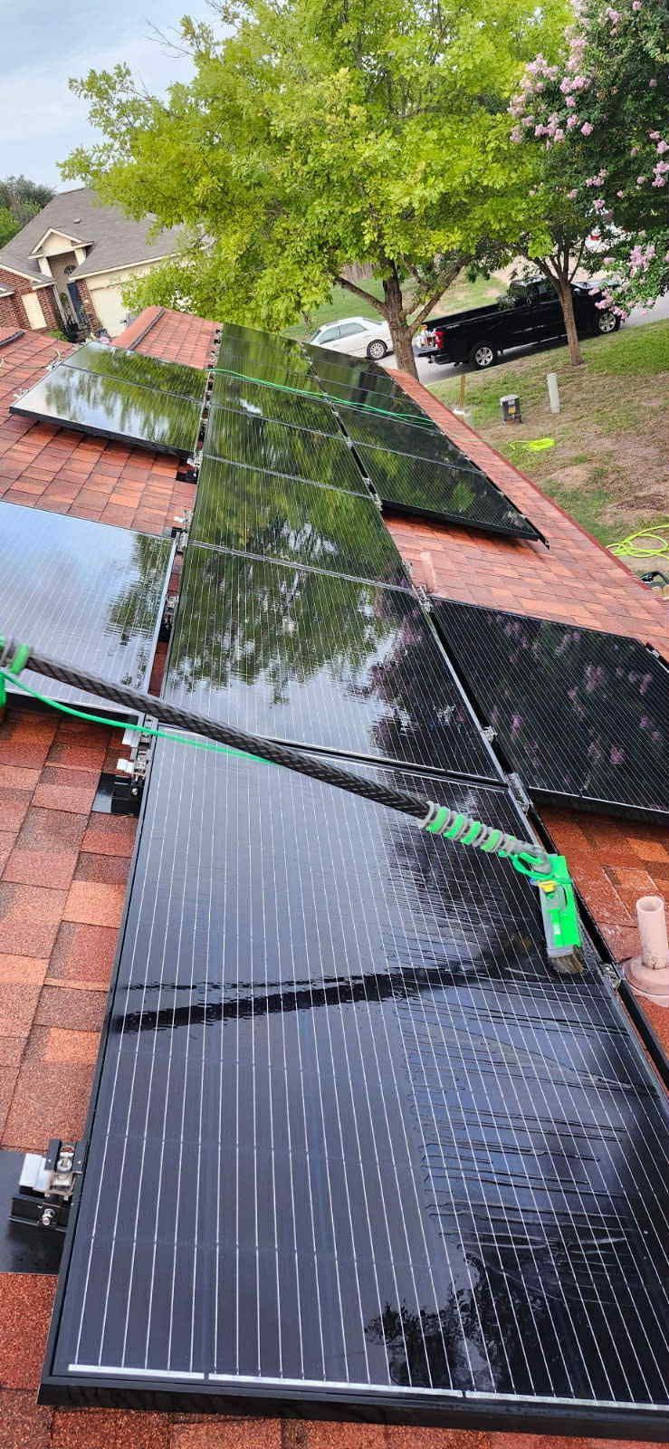 Solar panels being cleaned on a rooftop.  Green cleaning tool used on wet black panels and red roof.