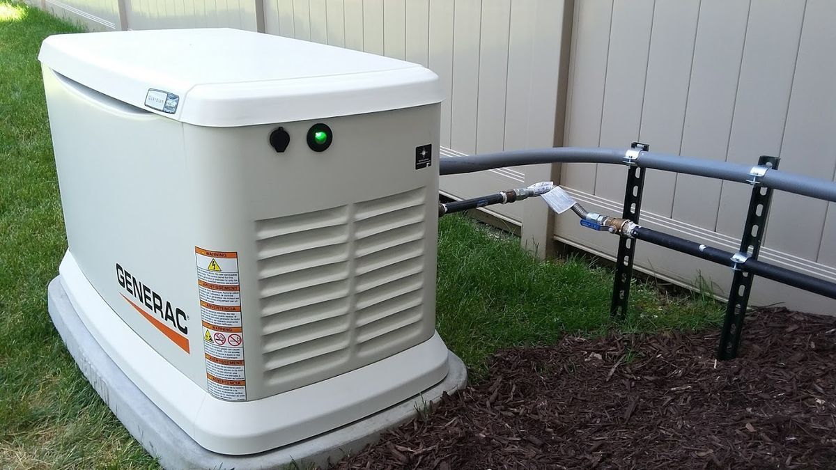 A generator is sitting in the grass next to a fence.