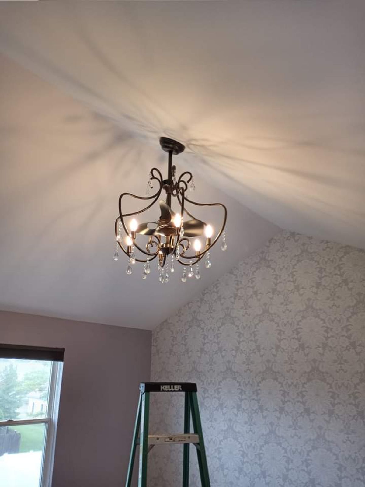 A chandelier is hanging from the ceiling in a room next to a ladder.