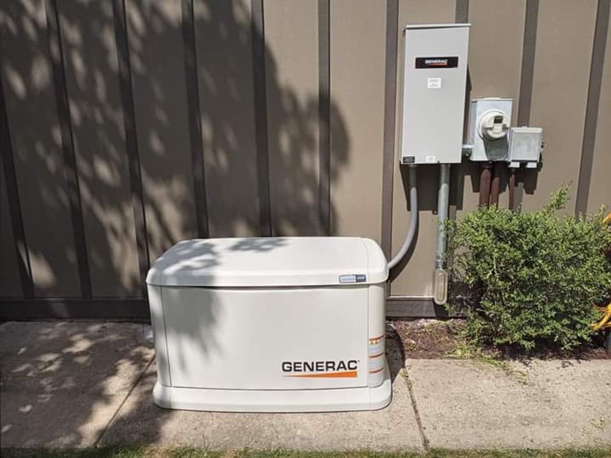 A generator is sitting on the sidewalk next to a wall.