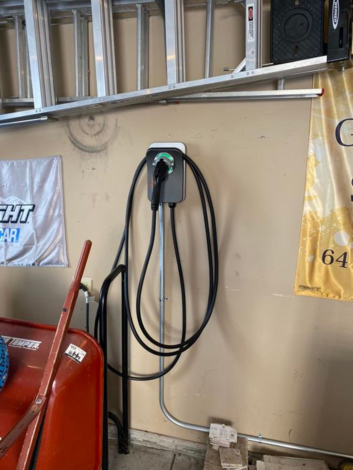 A charger is hanging on a wall in a garage next to a ladder.