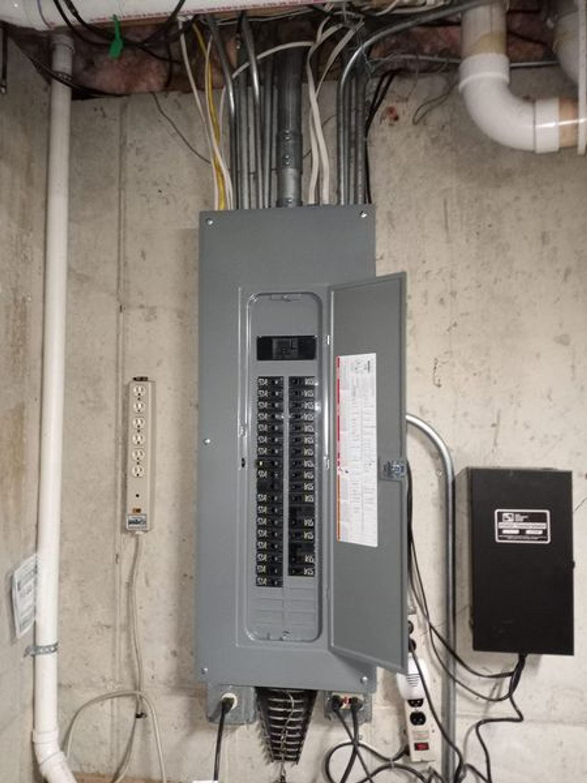 A electrical box is hanging on a wall in a basement.