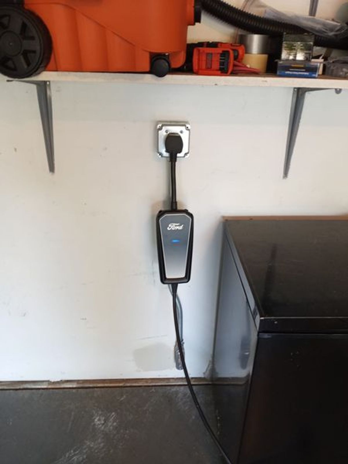 A ford charging station is attached to a wall in a garage.