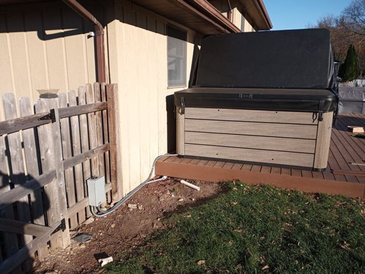 A hot tub is sitting on a deck next to a house.
