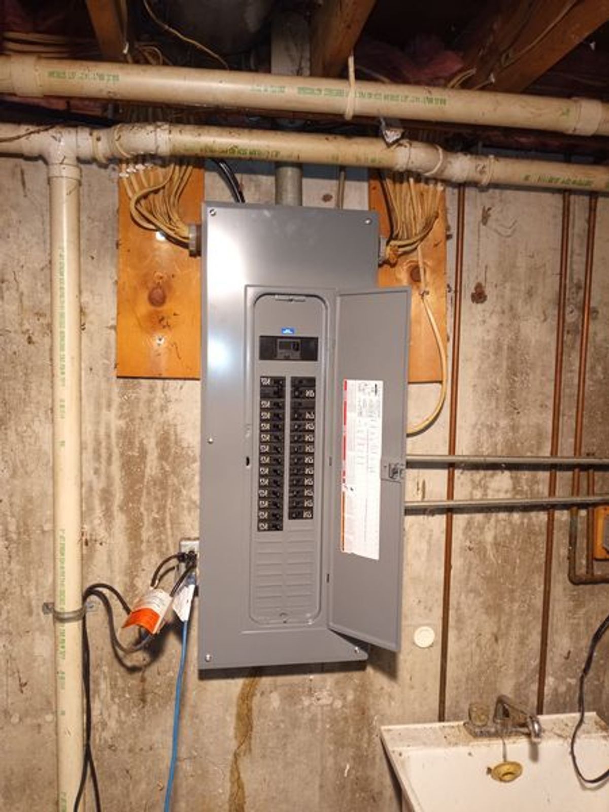 A electrical box is hanging on a wall in a basement.