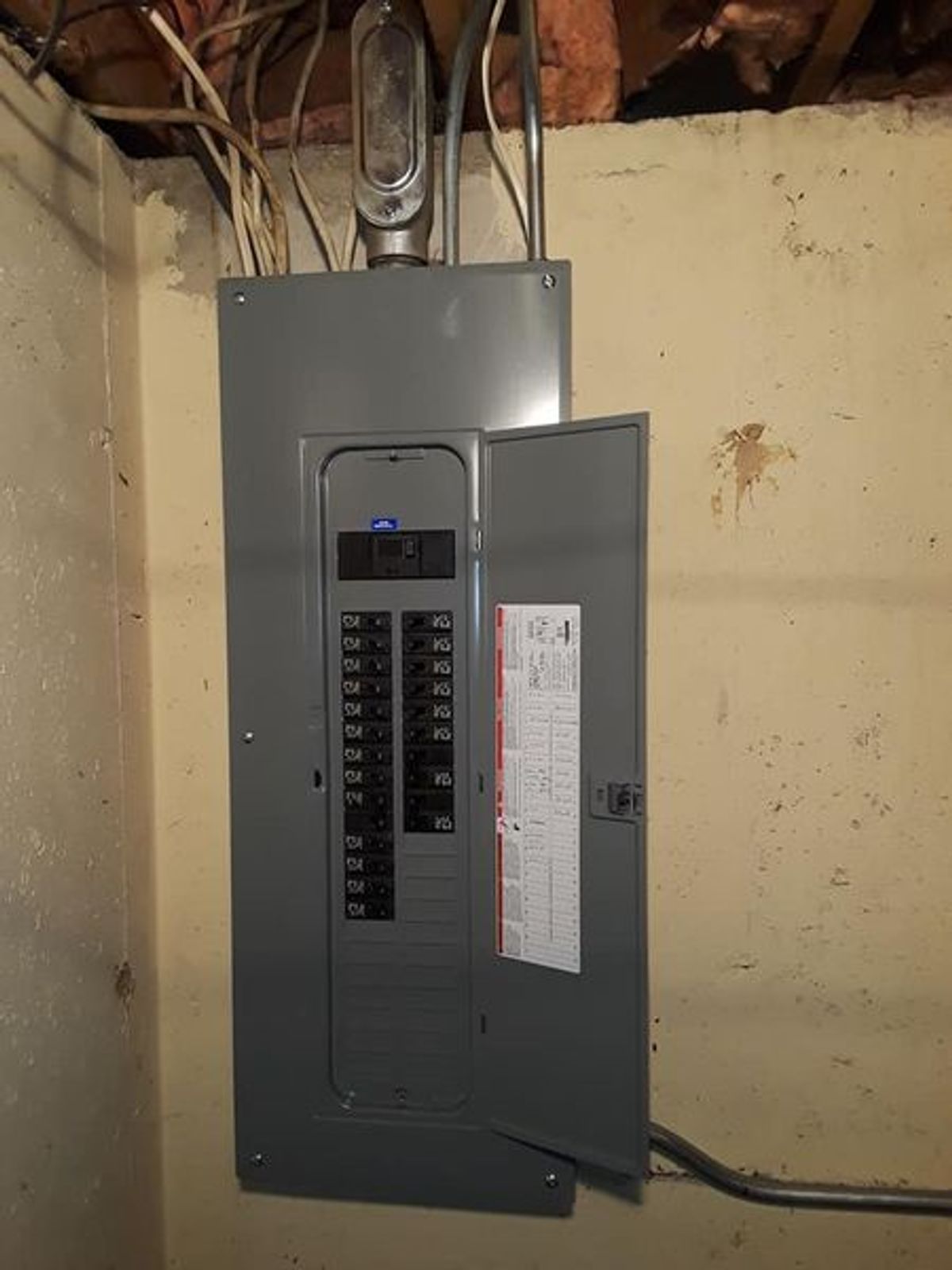 A electrical panel is hanging on a wall in a basement.