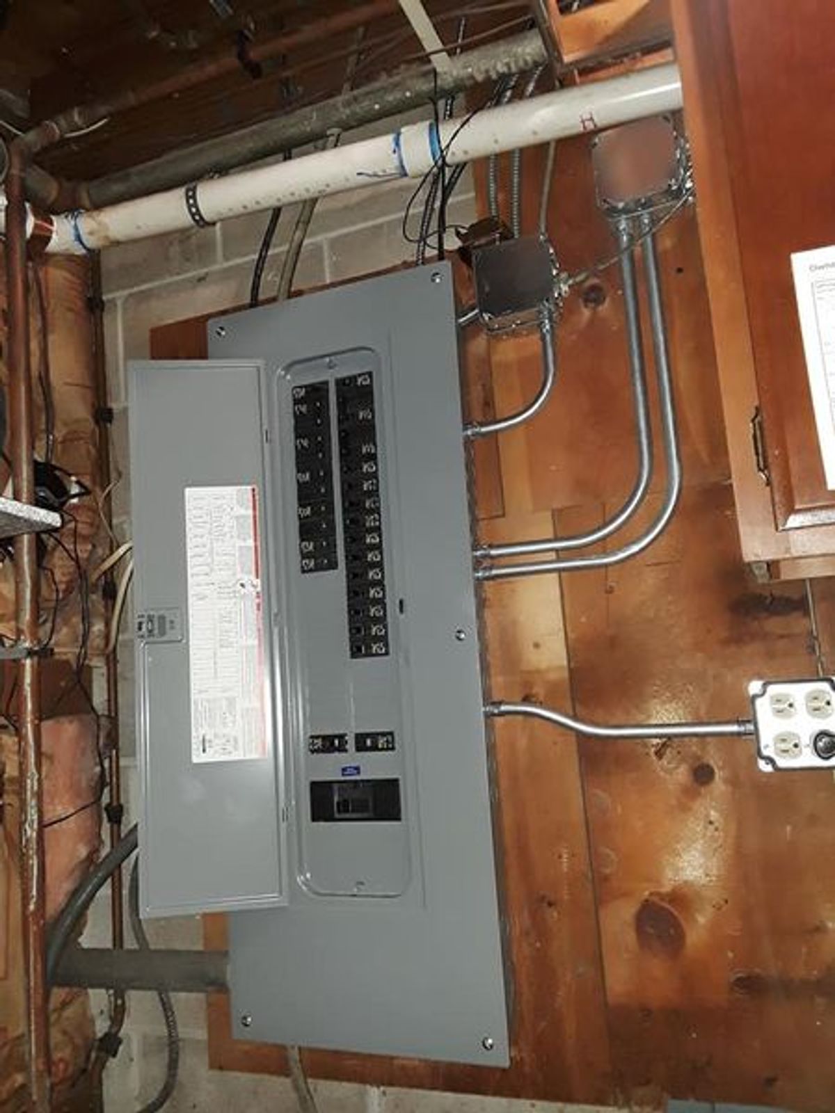 A electrical box is hanging on a wooden wall in a basement.
