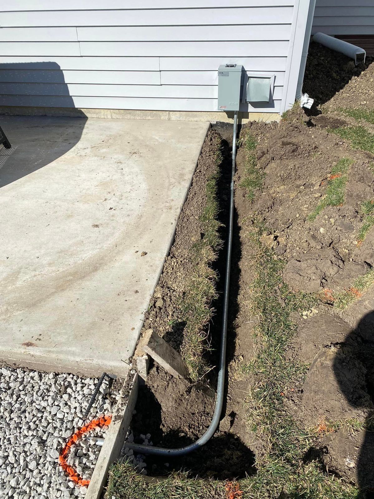 A power line is being installed in the dirt next to a house.
