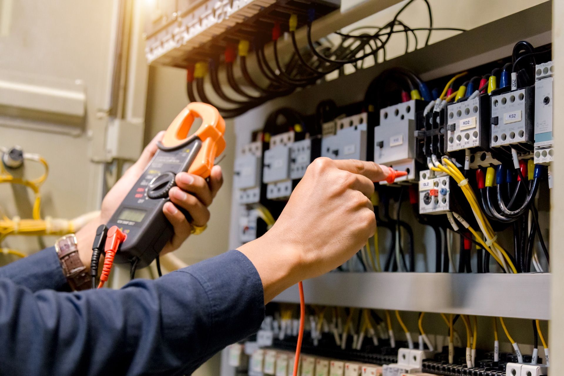 An electrician is working on an electrical panel with a clamp meter.