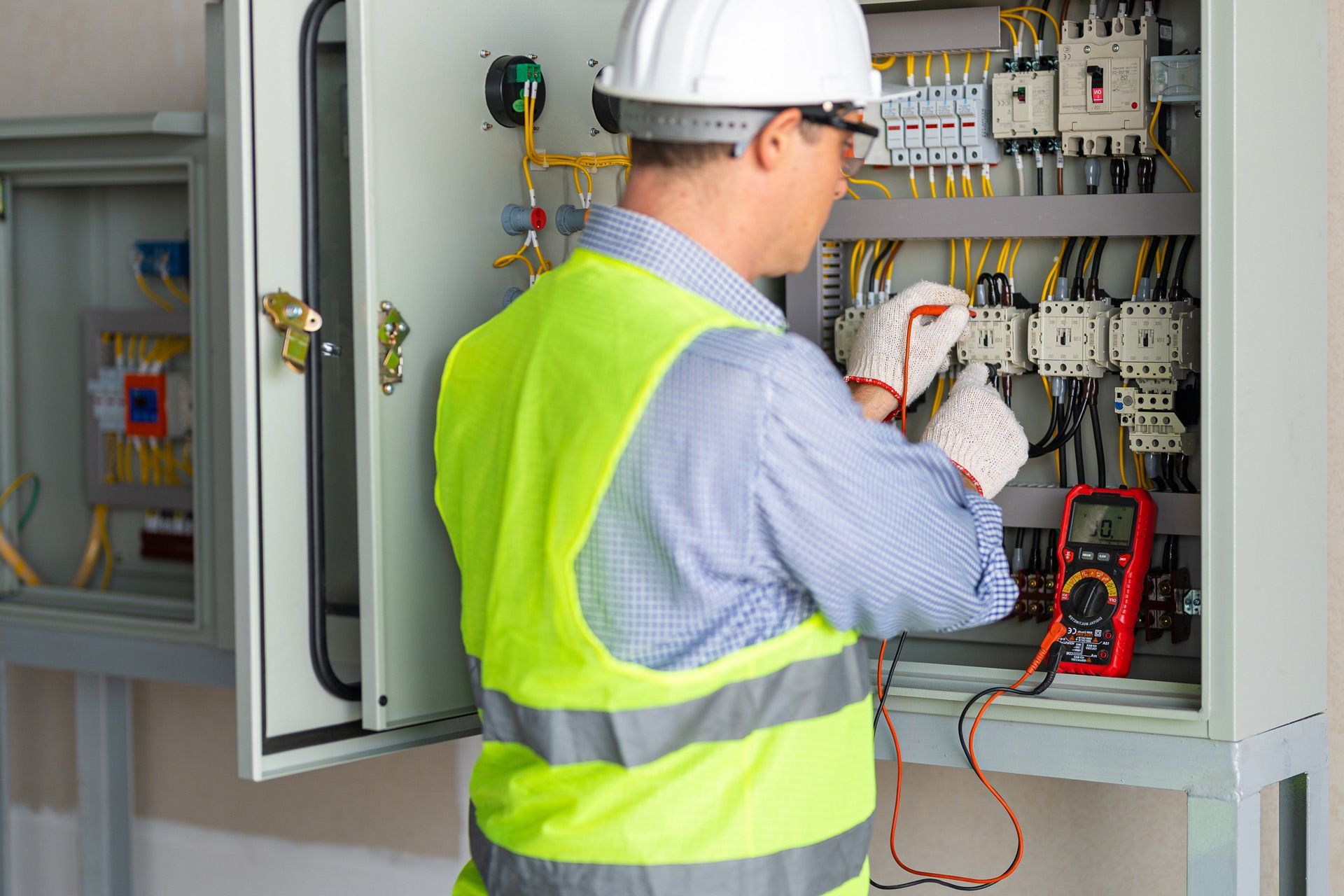 A man in a hard hat and safety vest is working on an electrical box.