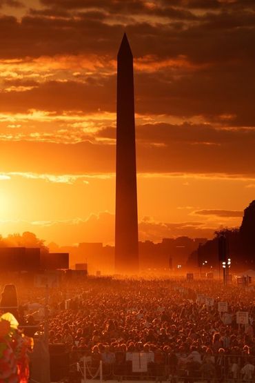 A large crowd is gathered in front of the washington monument at sunset