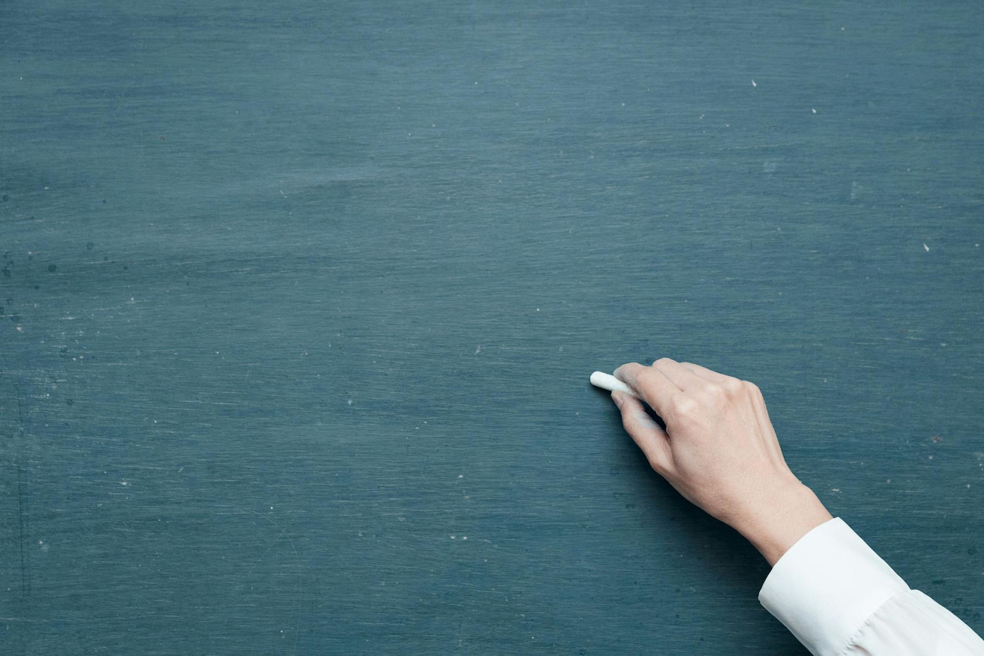 A person is writing on a school blackboard with chalk.