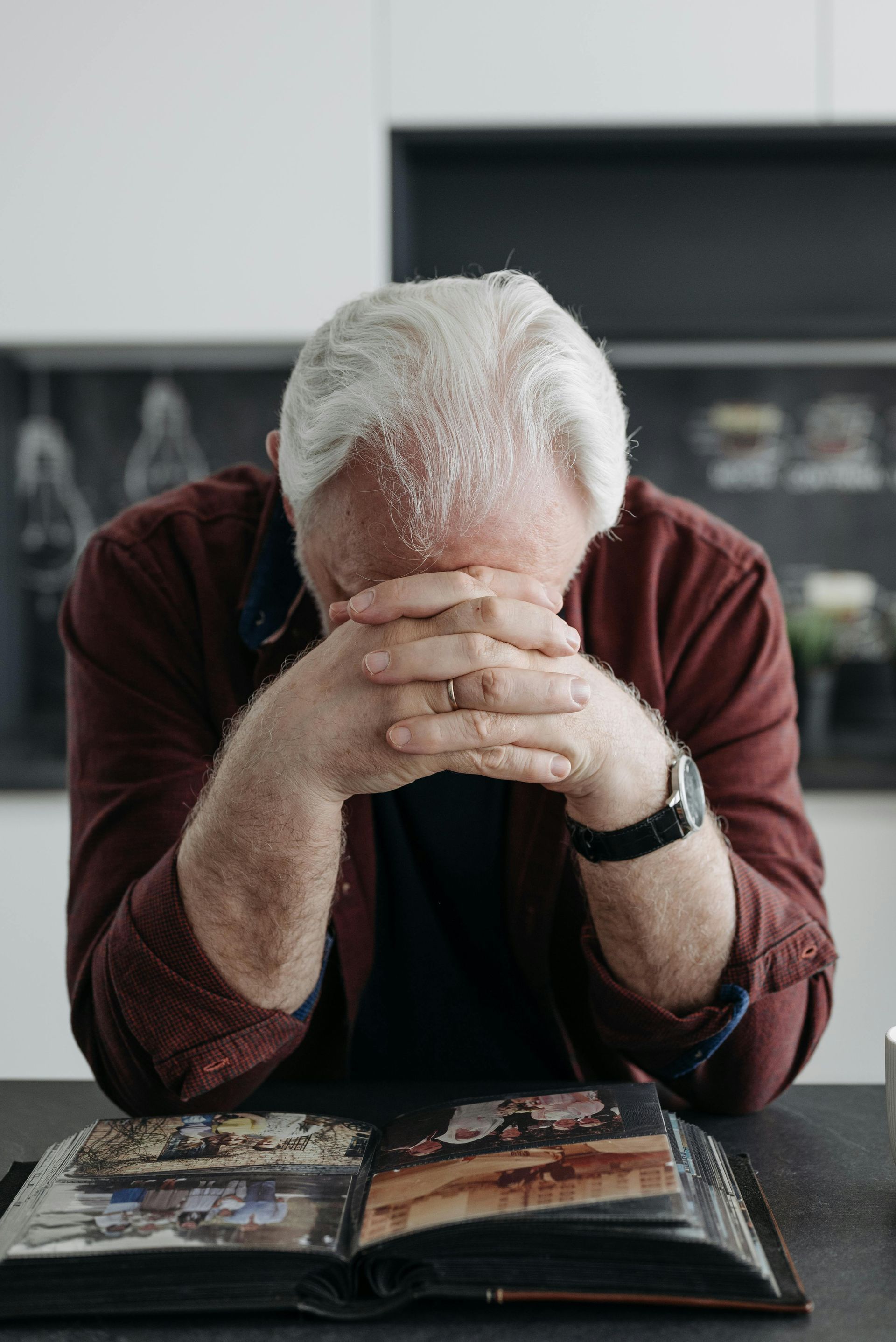 An older man is sitting at a table with his head in his hands suffering from dementia.