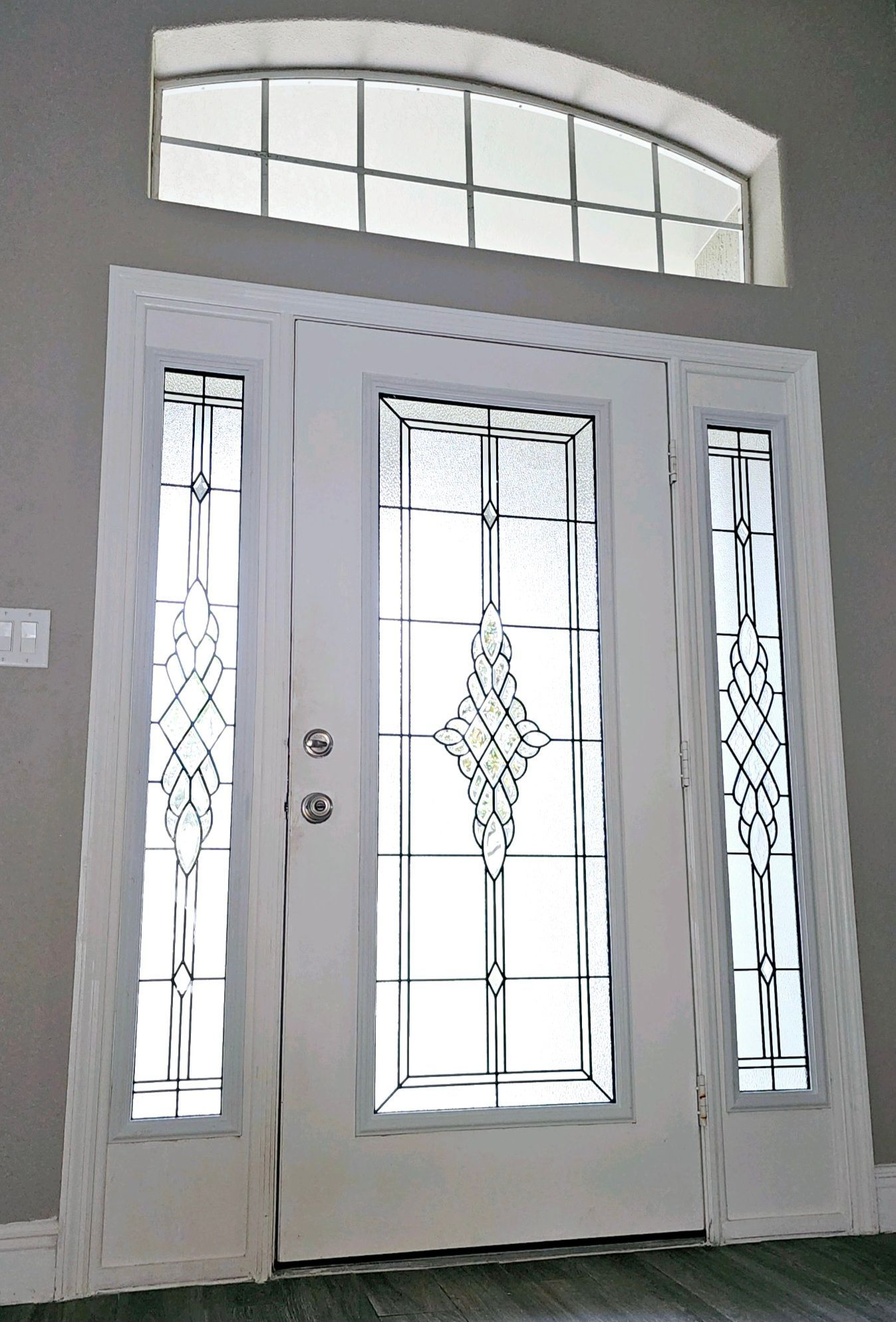 White entry door with decorative glass panes, side panels, and arched transom window.