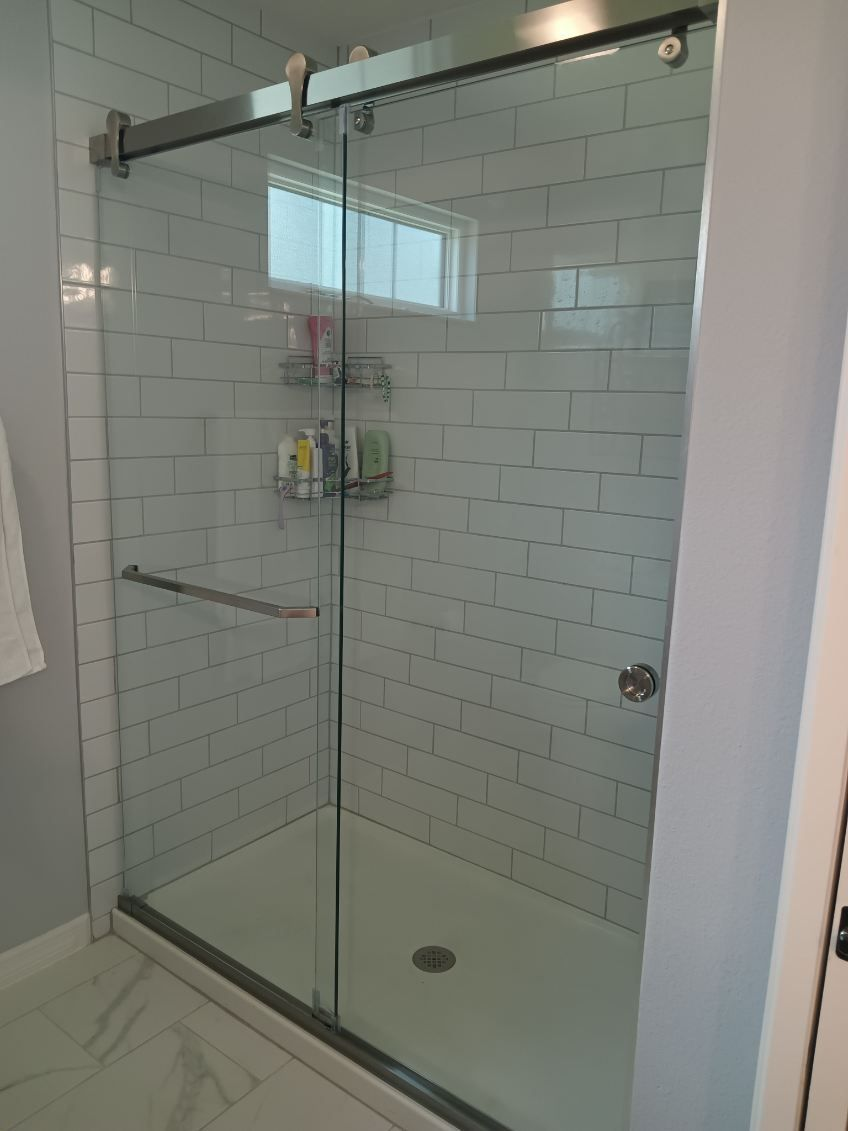 Glass shower enclosure with white subway tile, soap caddy, and sliding door with chrome hardware.