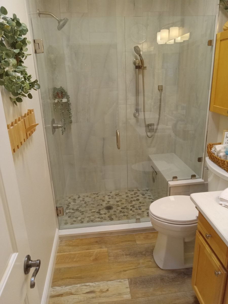 Bathroom with glass shower, river rock floor, wooden floor, and a toilet.