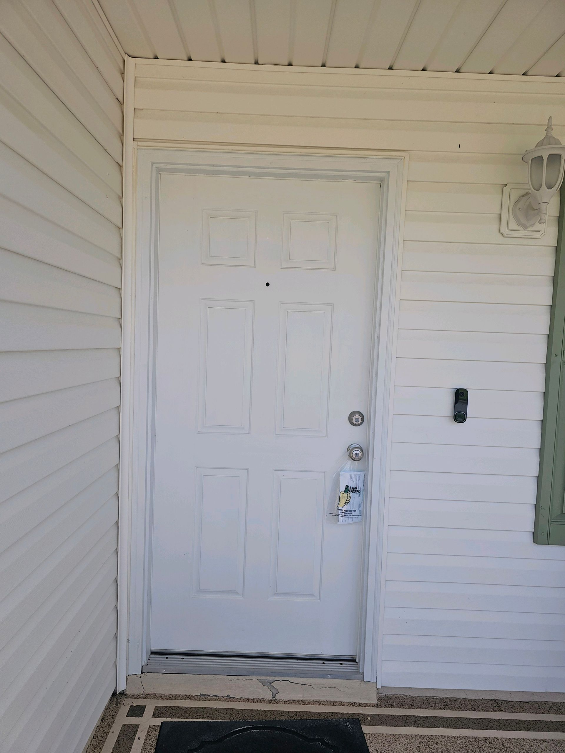 White front door with lock, doorbell, and sidelight, set in a white siding exterior.