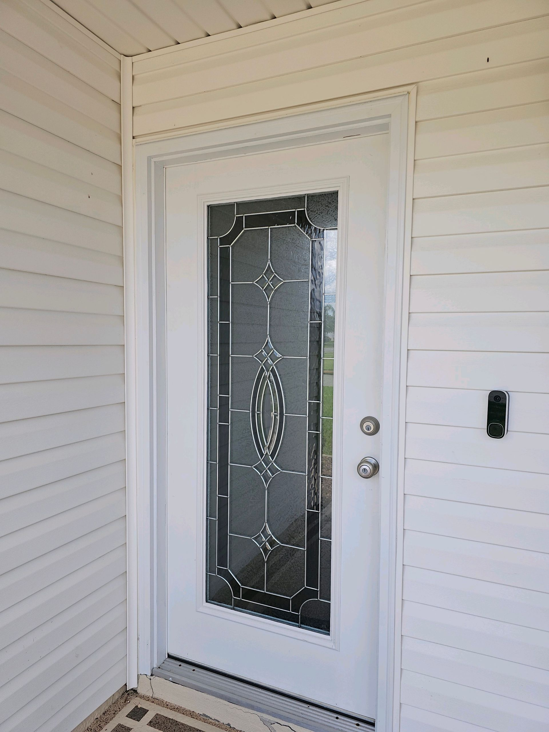 White front door with decorative glass panel, set into white siding.