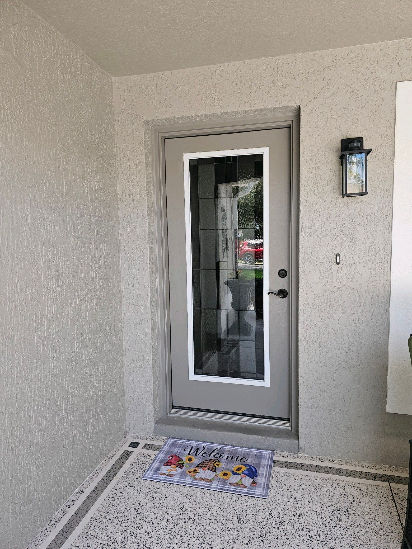 Exterior doorway with light gray door and textured walls. Welcome mat on the step.