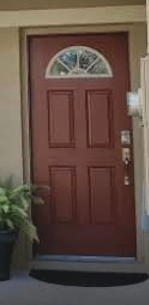 A reddish-brown front door with a semi-circle window at the top, surrounded by beige walls.