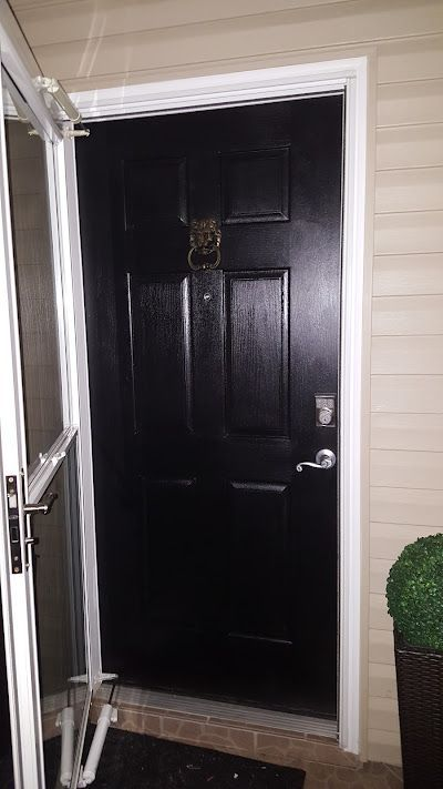 Black front door with a gold door knocker, open screen door, beige siding.