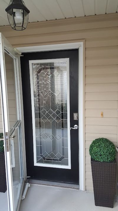 Black door with decorative glass panel, open glass storm door. Brown wicker planters with green topiary.
