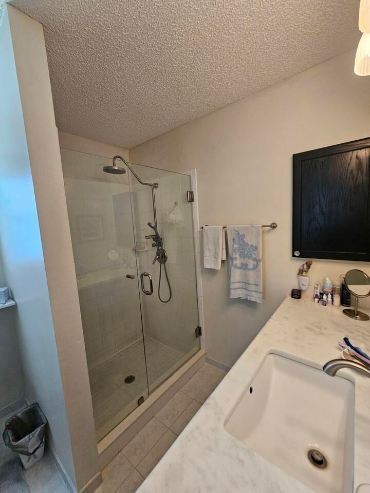 Bathroom with glass shower, white sink, and black mirror. Neutral colors.