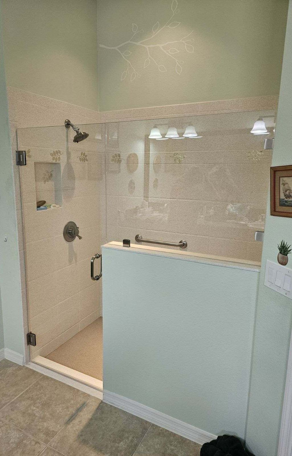 Glass-walled shower with light-colored tile walls. Features a shower head, fixtures, and half wall.