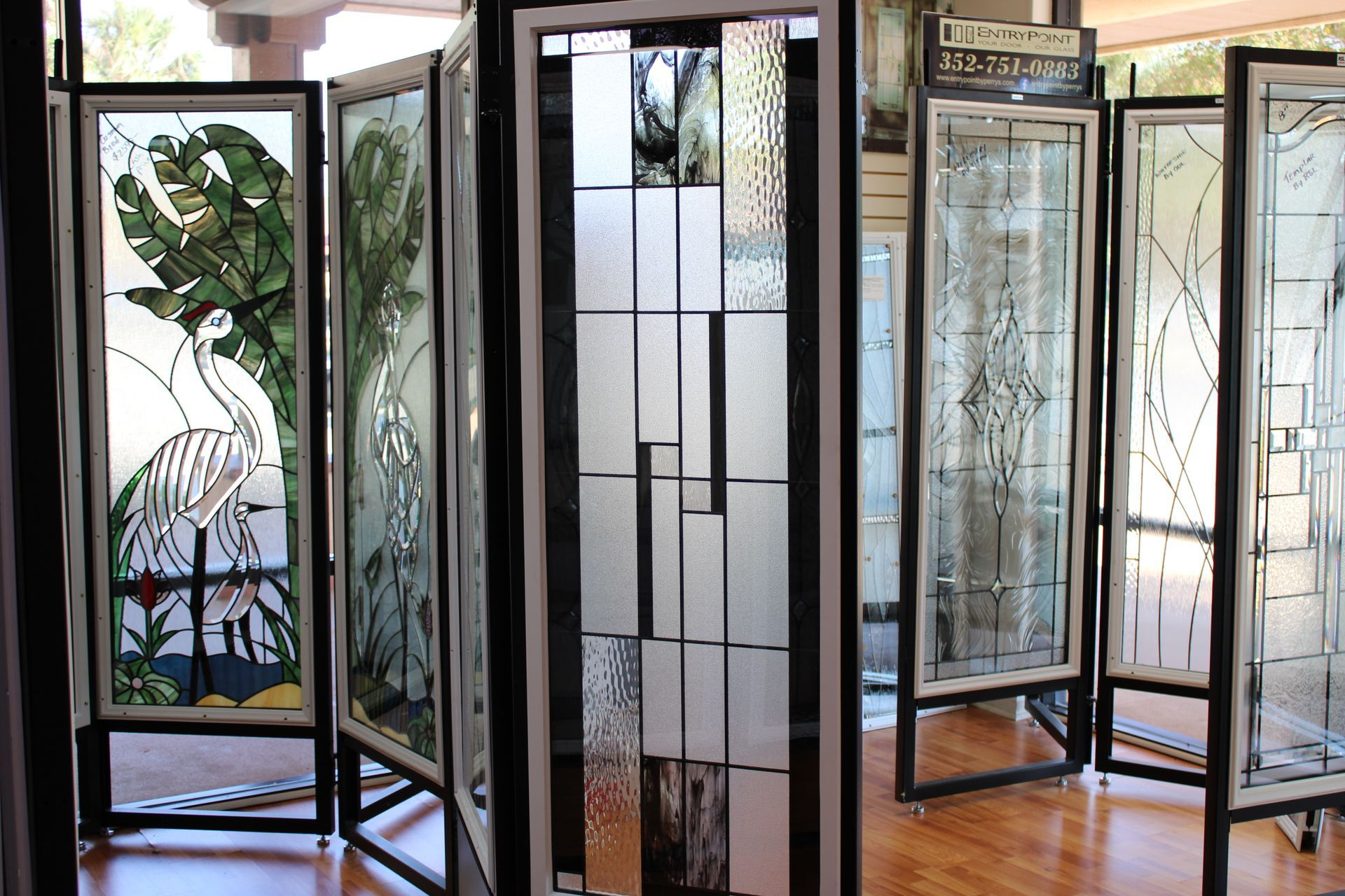 Folding screens with stained glass panels, showcasing various designs, standing on a hardwood floor.