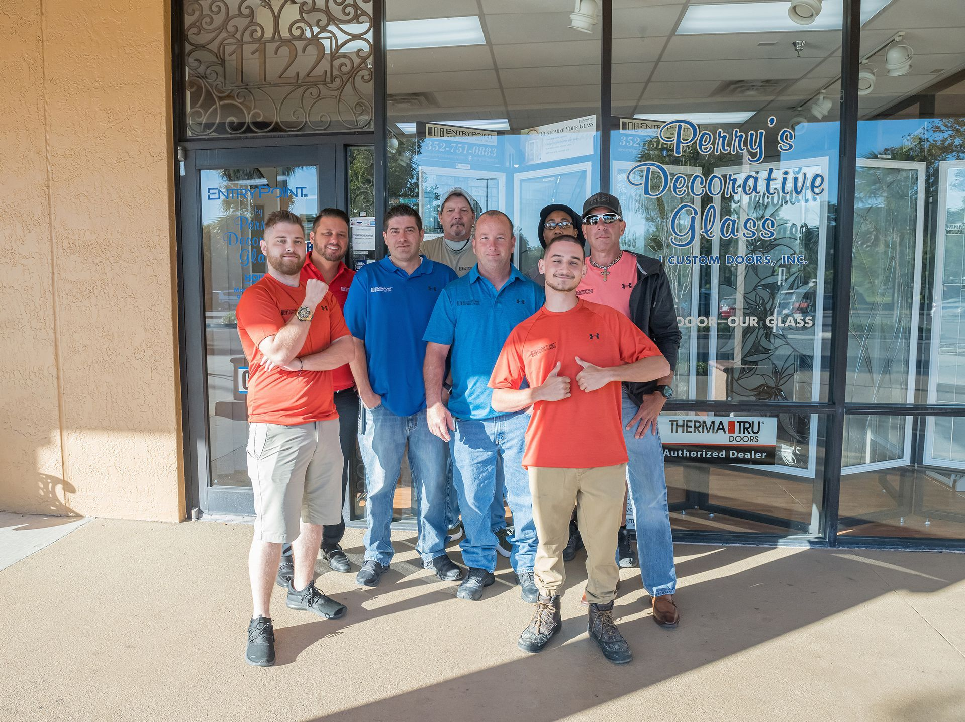 Group of men standing in front of a glass door; one gives a thumbs up. Exterior shot.