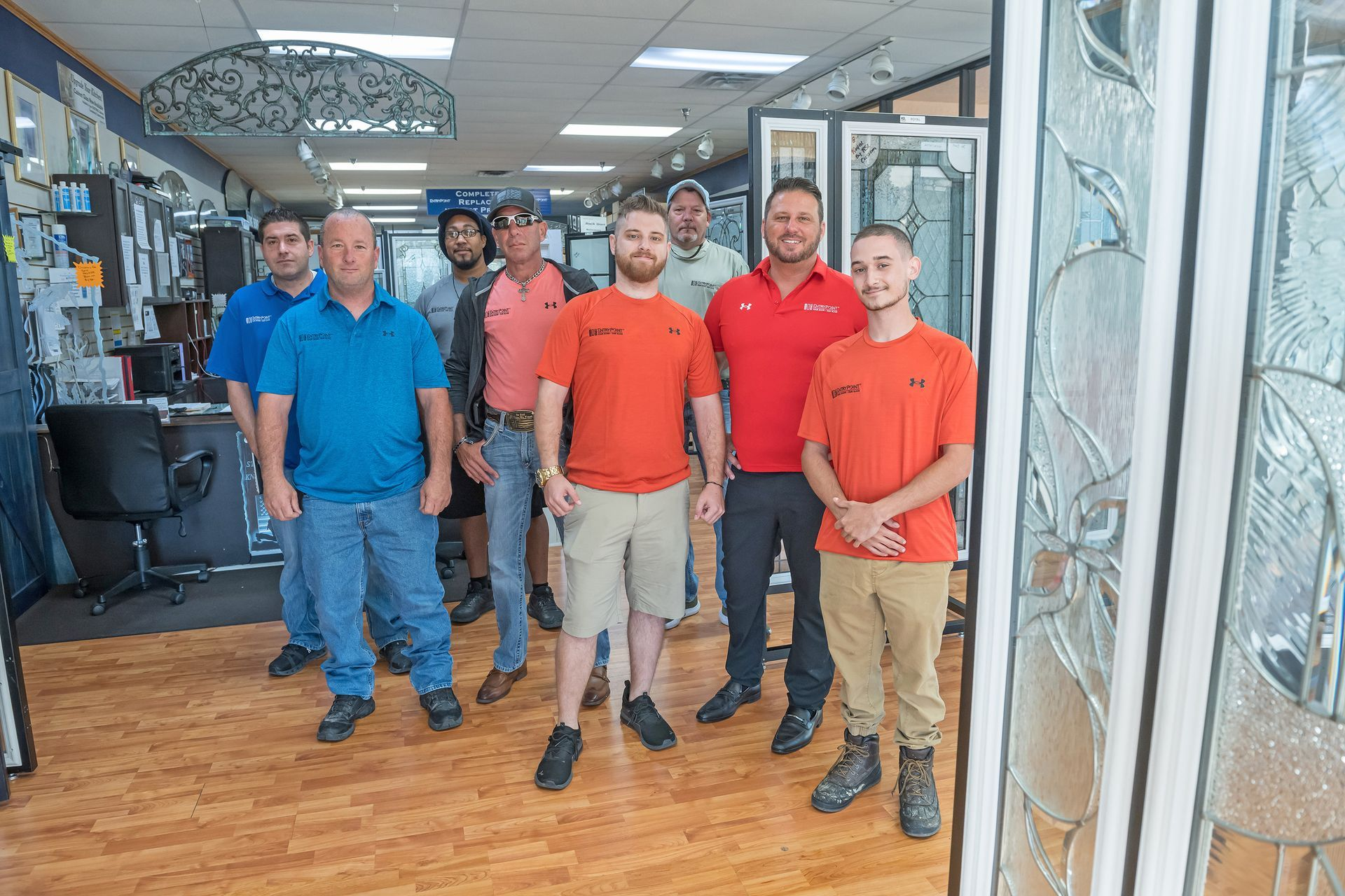 Group of men in a showroom, some wearing orange shirts, standing near glass doors.