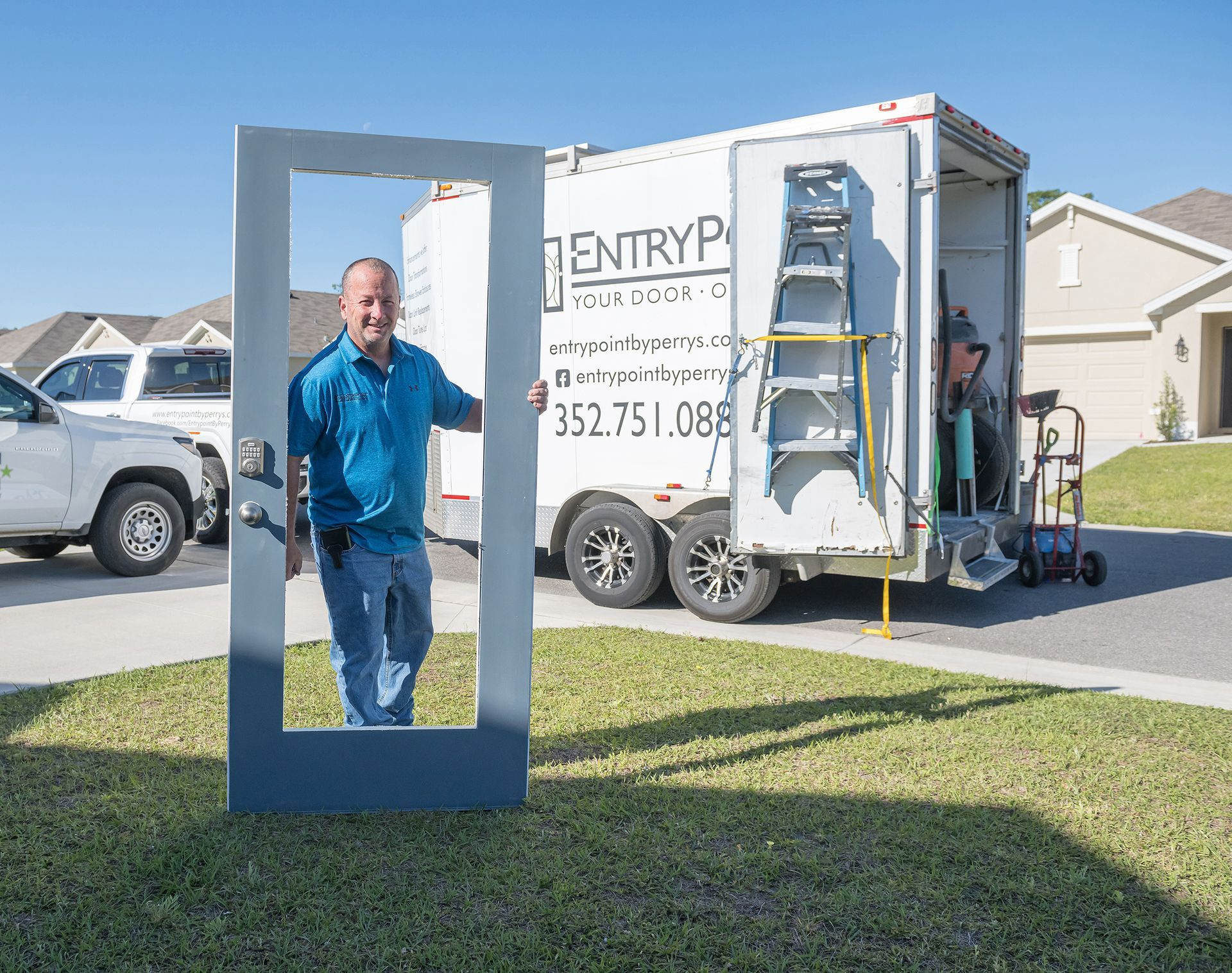 Man holds up a gray door frame on a lawn. A truck with "ENTRY PRO" logo is behind him, with another person inside.