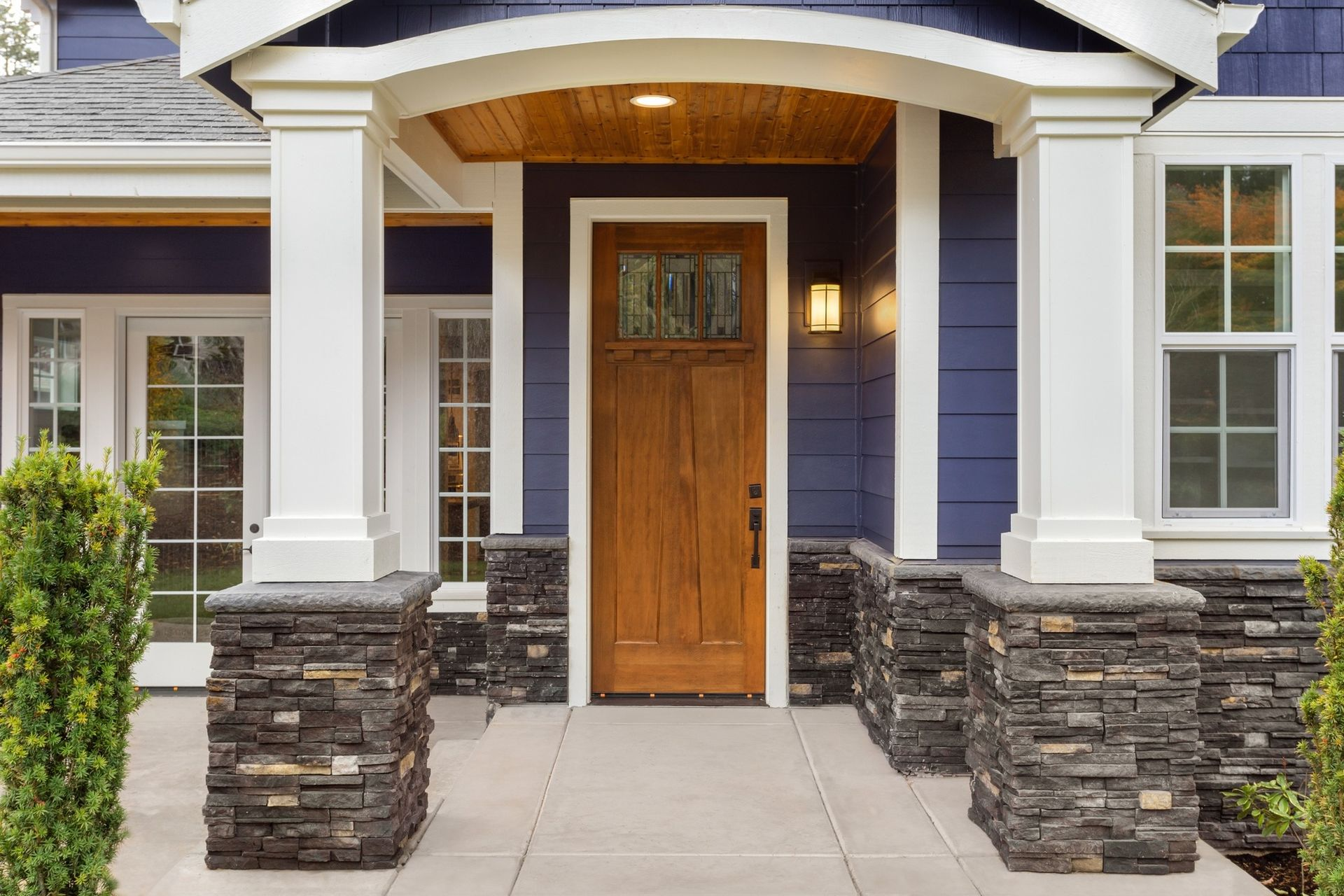 Front entrance of a blue house with white pillars and stone accents, wooden door.