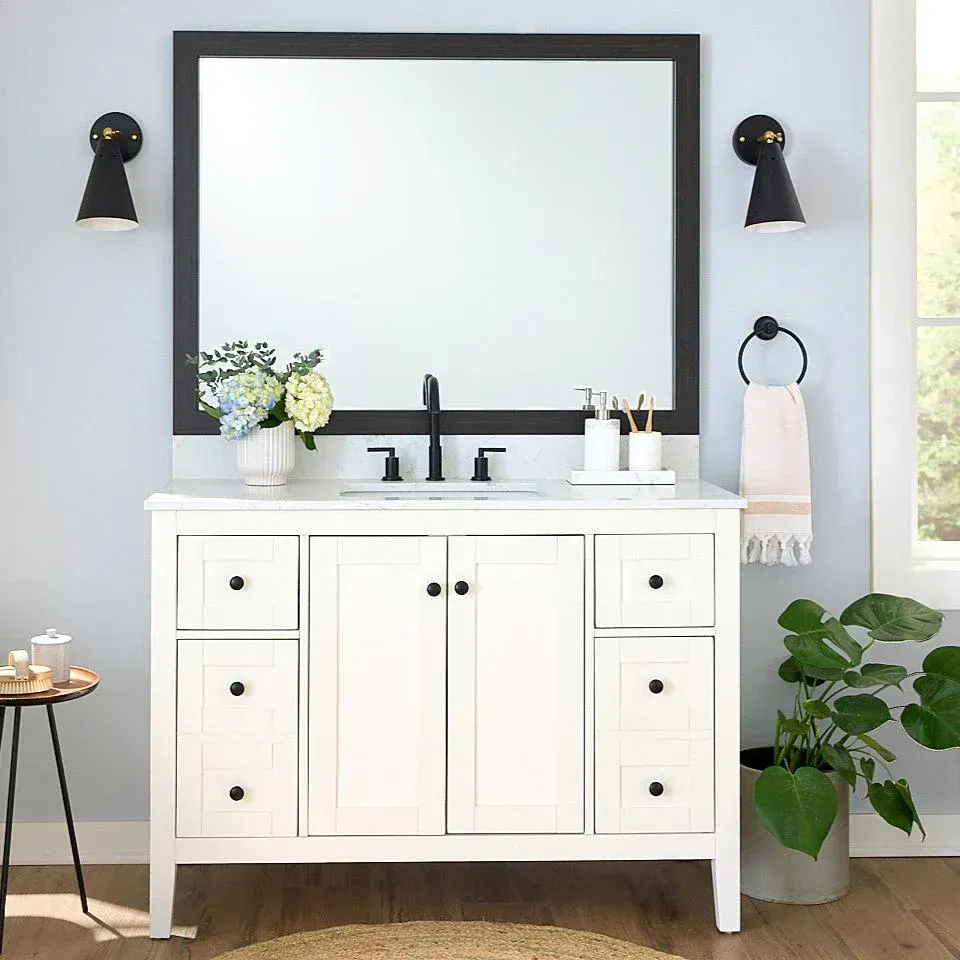 White bathroom vanity with mirror, sconces, and decor, on a light blue wall.