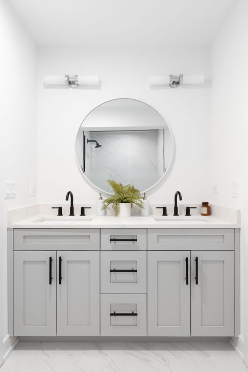 Modern bathroom with a light gray double vanity, round mirror, and black fixtures.