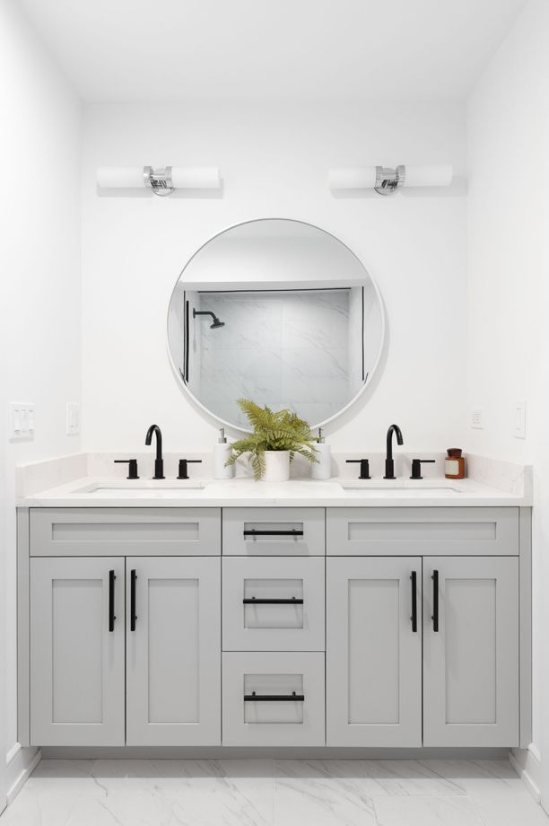 Modern bathroom with a light gray double vanity, round mirror, and black fixtures.