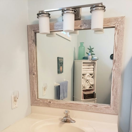 Bathroom mirror with wood frame, light fixture above, and sink below.