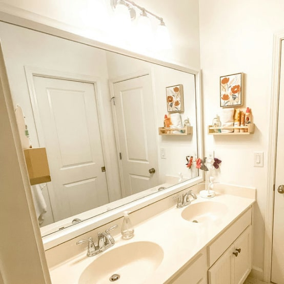 Bathroom with large mirror over double sinks, two doors, and wall art. White and beige tones.