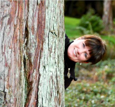 A woman peeking out from behind a tree trunk