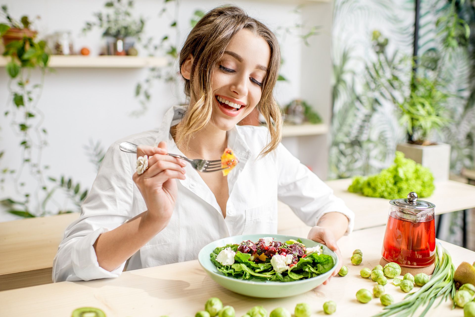 A woman is sitting at a table eating a salad with a fork.